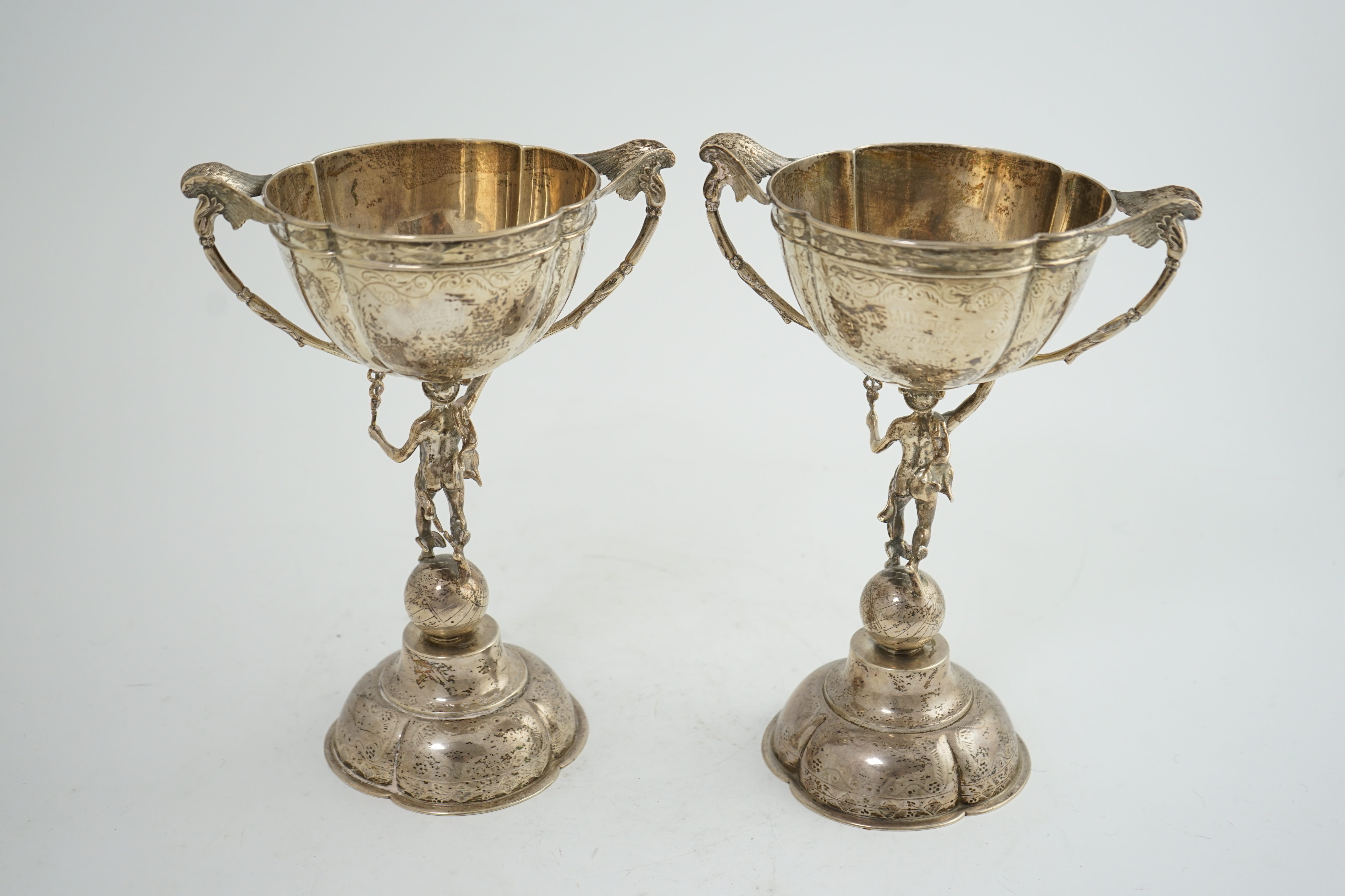 A pair of Victorian silver two handled pedestal cups, each figural stem modelled as Hermes upon a globe, by Edward Charles Brown